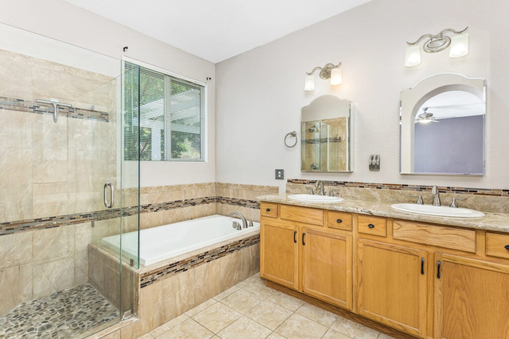 Primary ensuite bath with dual vanities, glass shower, and soaking tub — DeBonis Real Estate Team]